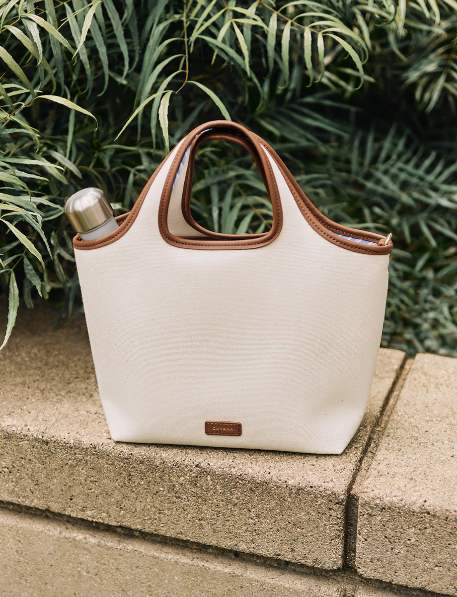 Tote bag with a bottle inside, placed on a stone ledge, with plants in the background.