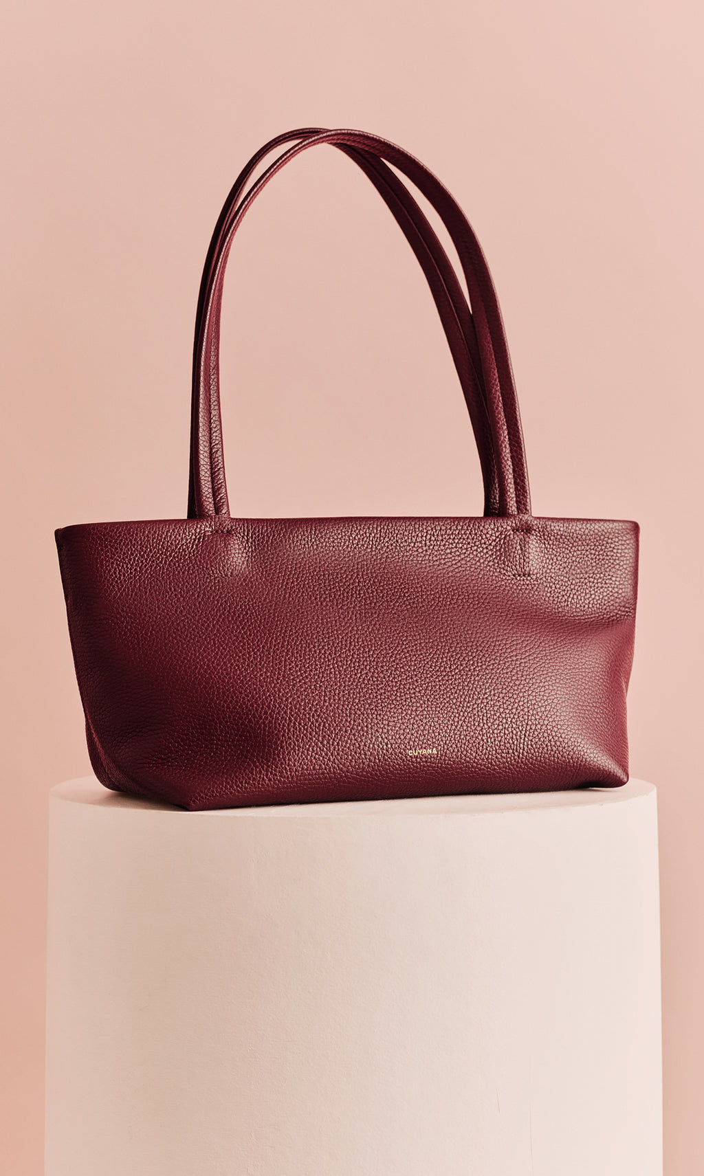 Handbag with two straps on a cylindrical pedestal.