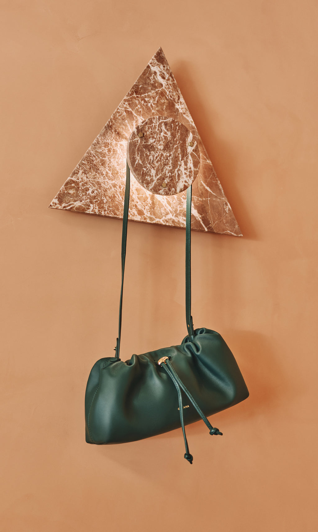 Handbag with long straps hanging on marble wall decoration