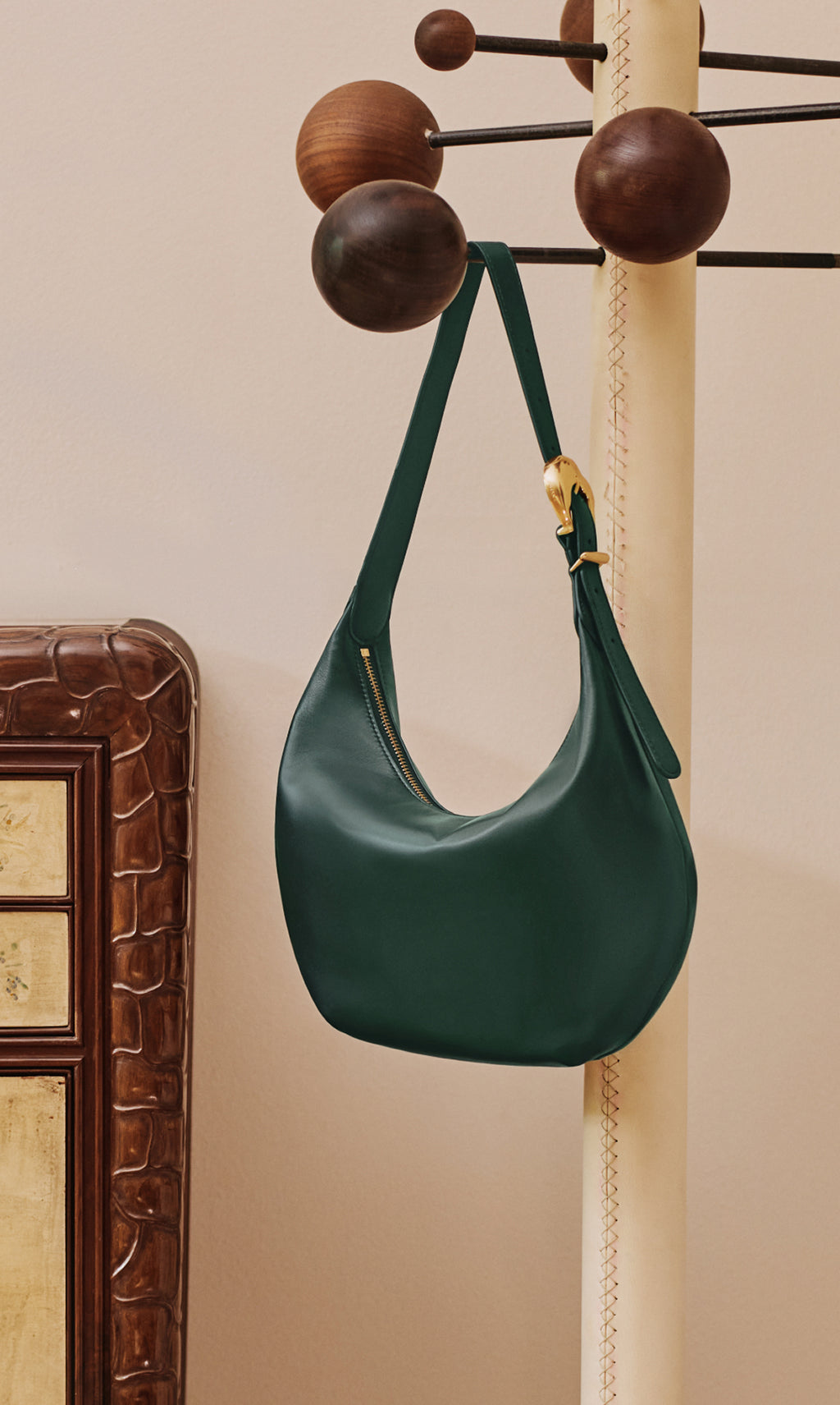 A handbag hanging on a stand near a decorative furniture piece.