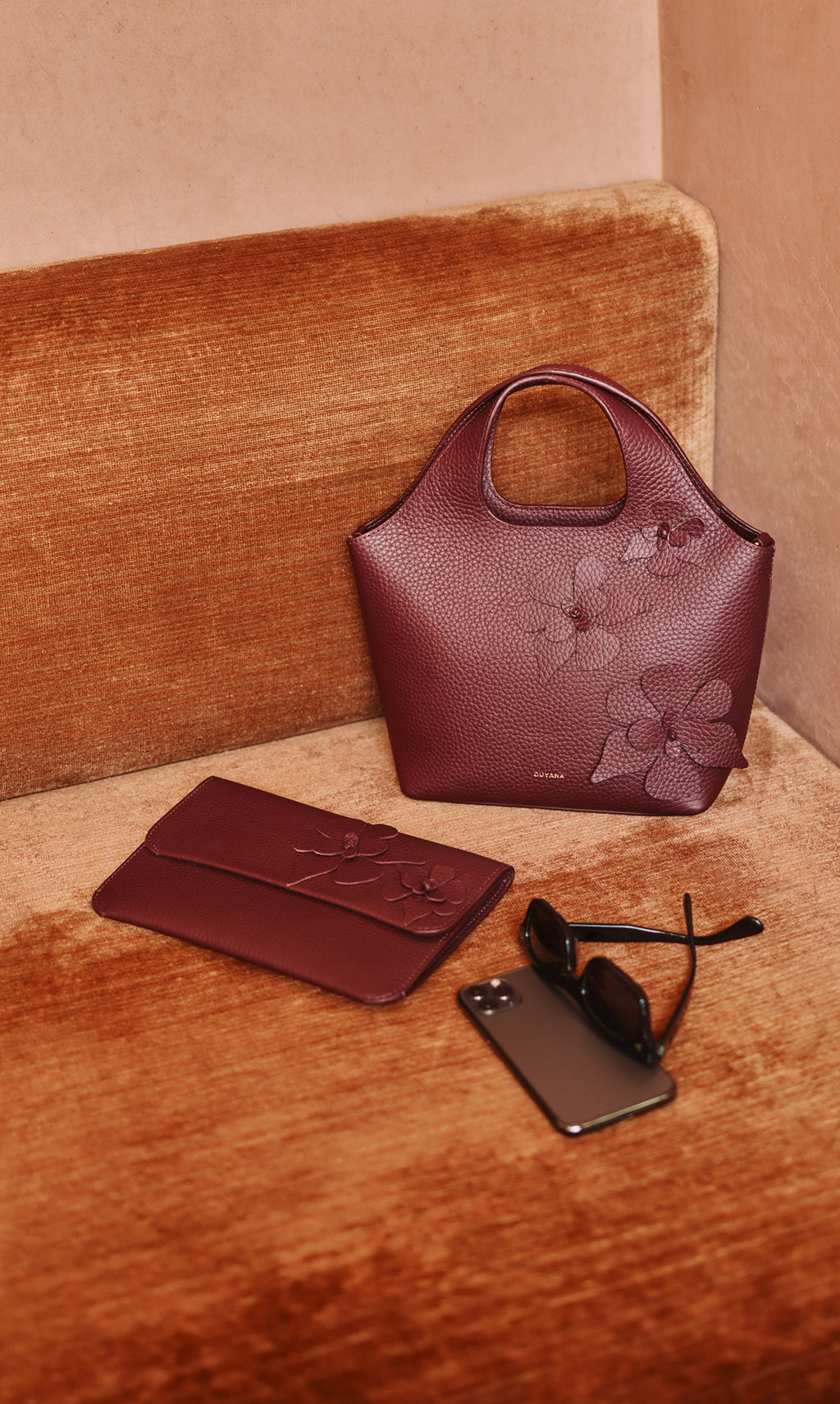 Handbag and clutch on sofa with sunglasses and a phone nearby.