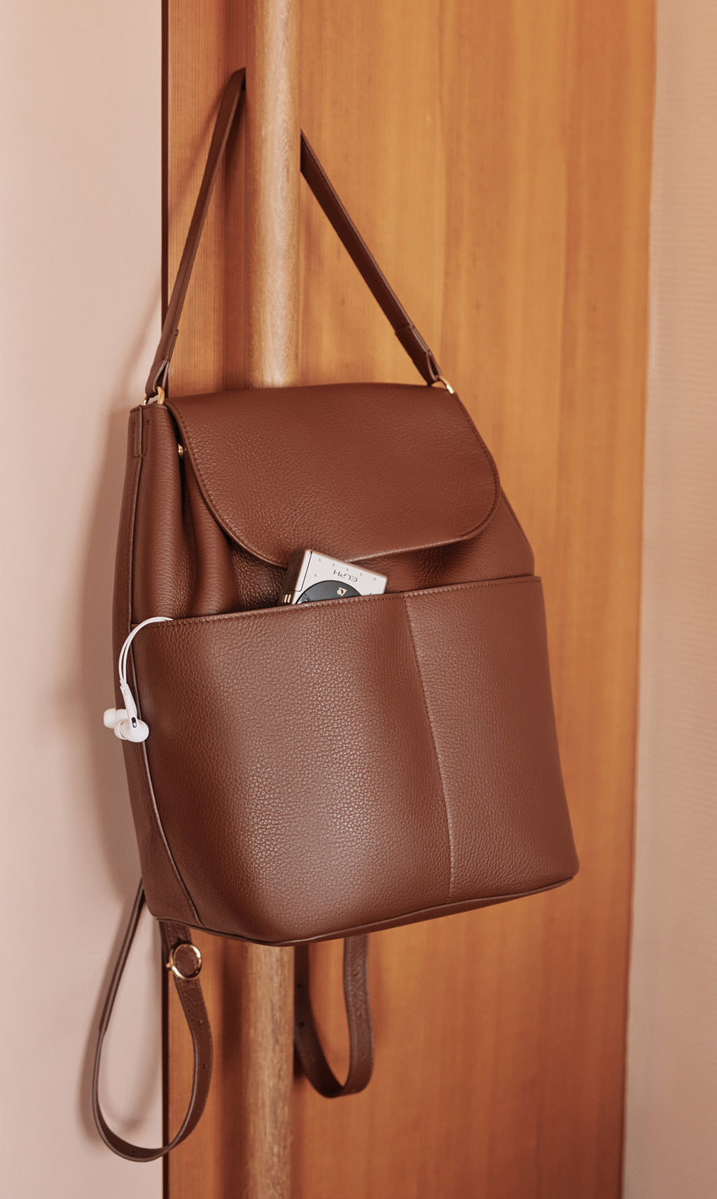 Backpack with phone and headphones in front pocket hanging on wall.