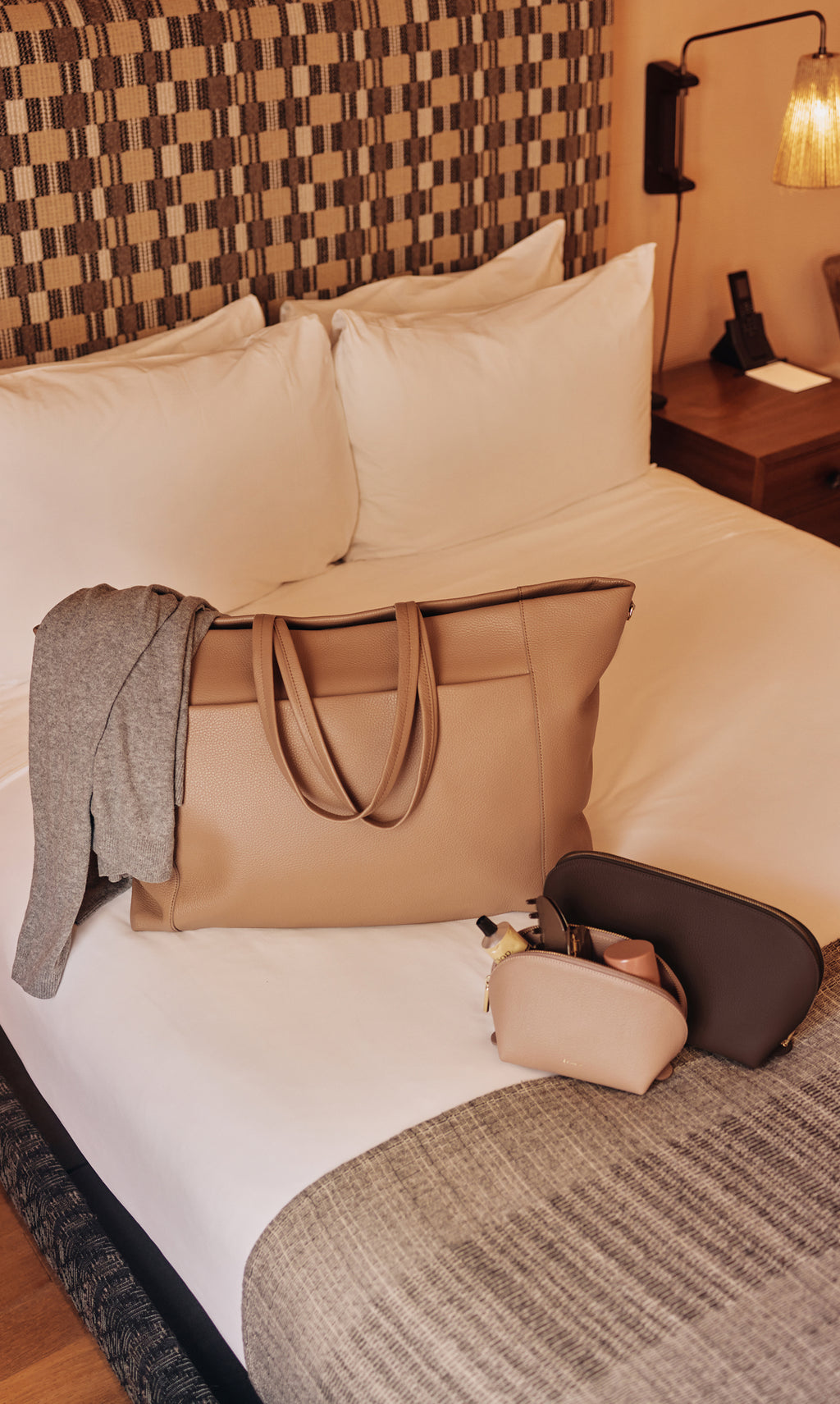 Travel bag and smaller bags on bed with sweater draped over travel bag.
