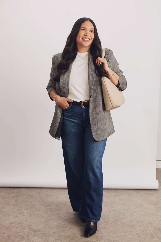 Person wearing a blazer and jeans, holding a handbag.