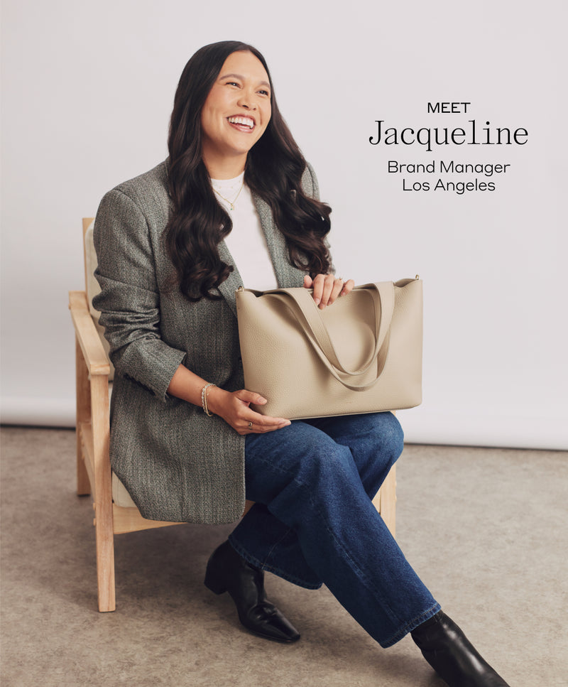 Person seated on chair holding a large handbag and smiling at the camera.