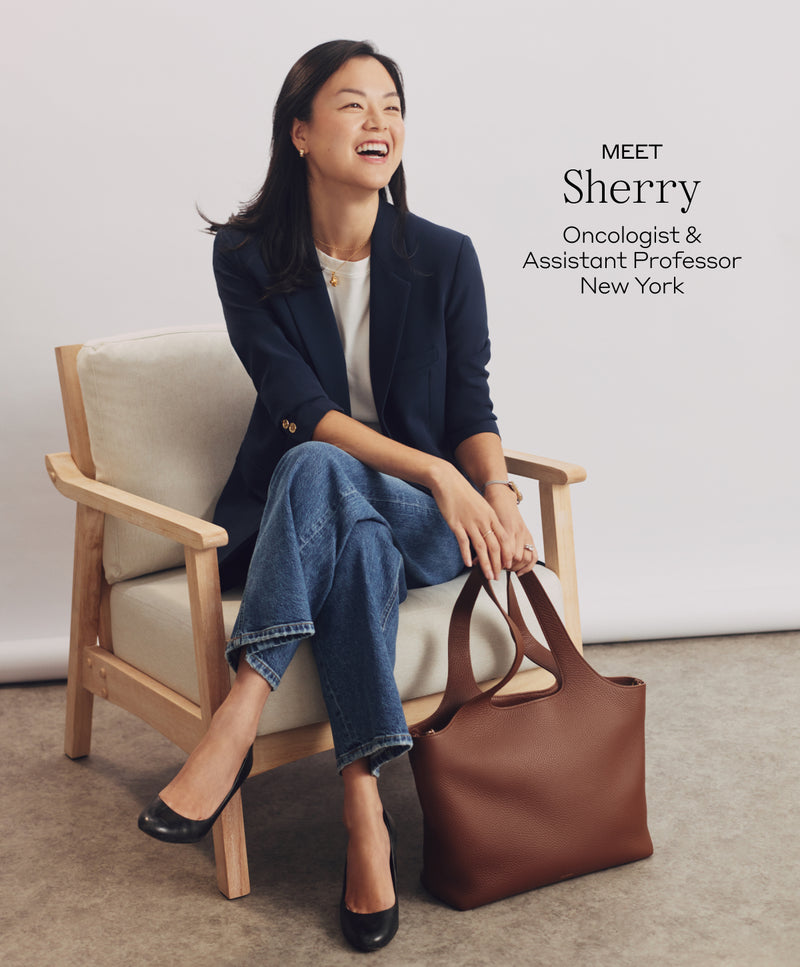 Person seated on chair smiling, holding a handbag.