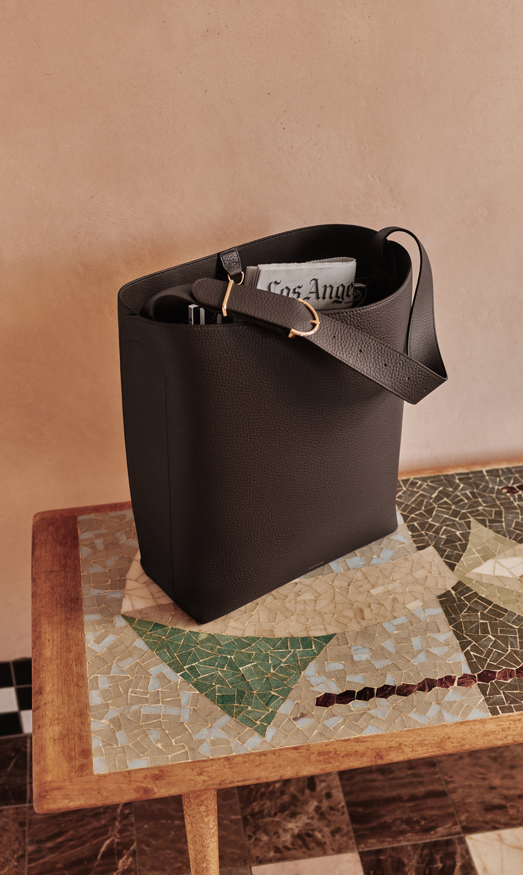 Tote bag on mosaic table holding a newspaper and items inside.