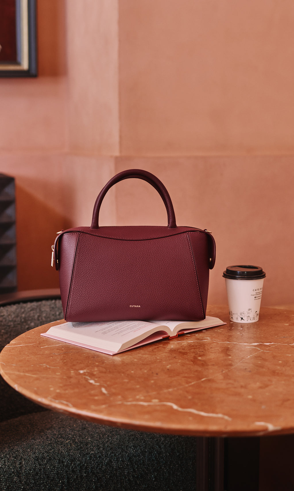 Handbag on an open book beside a coffee cup on a round table