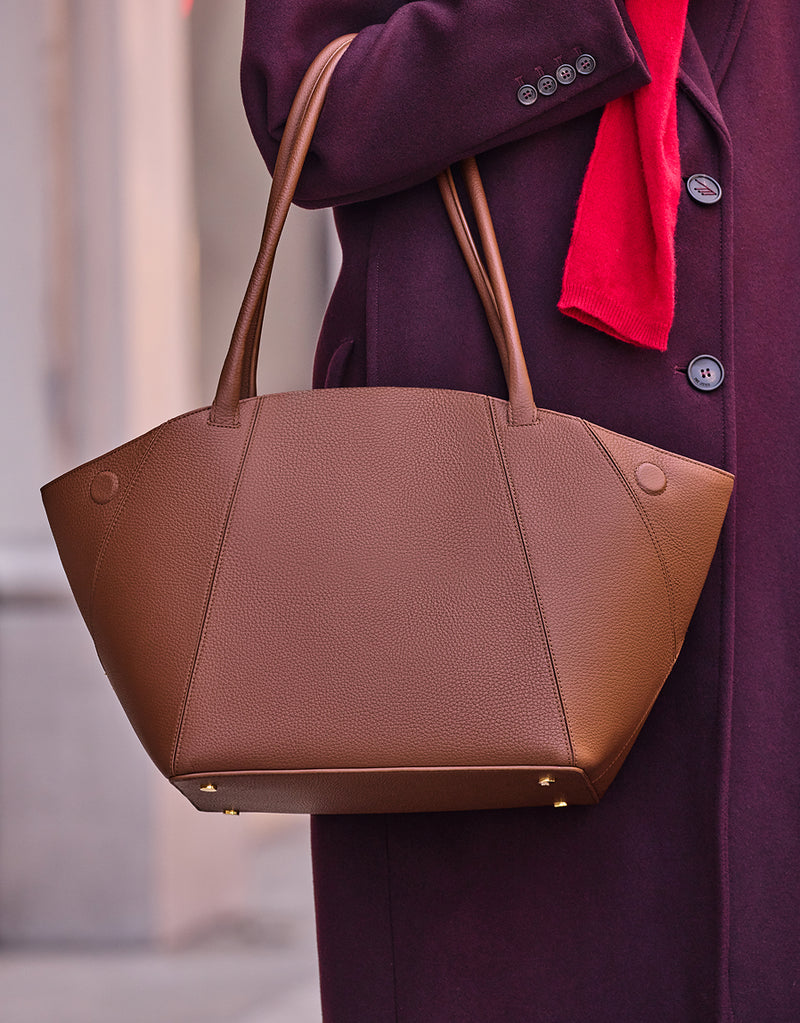 Person holding a large tote bag with long handles wearing a coat