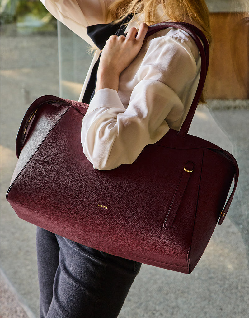 Person holding a large handbag with shoulder strap near a glass window.