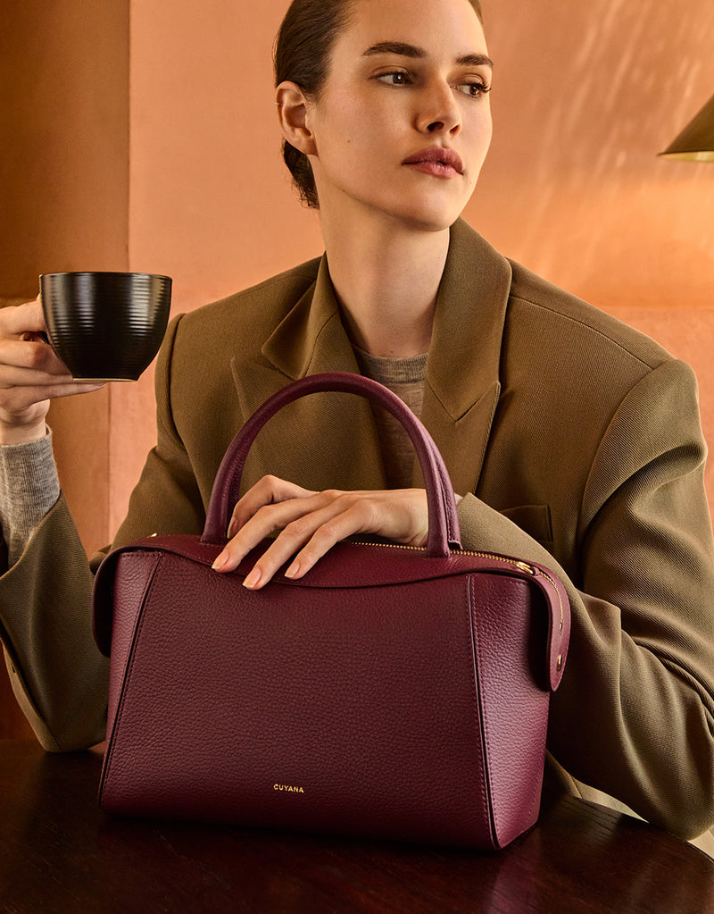 Person seated at table holds cup and purple handbag