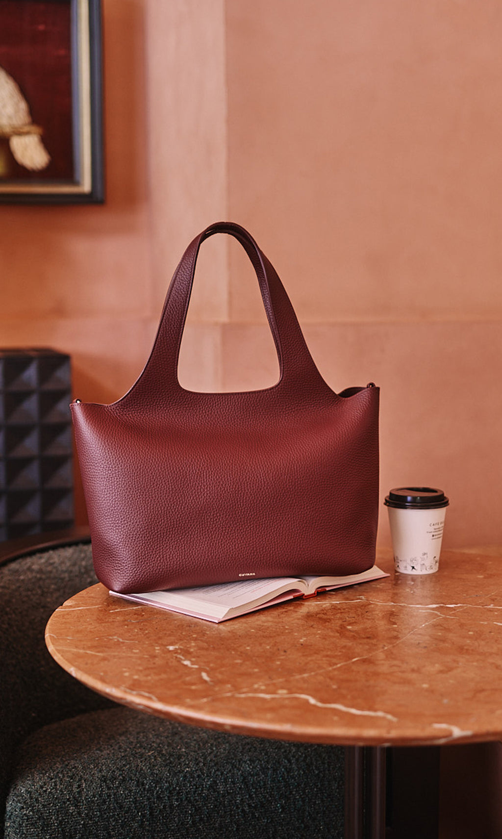 Tote bag on a table next to an open book and a coffee cup.