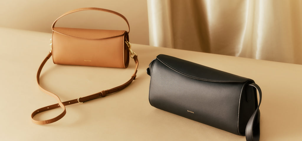 Two handbags on a flat surface with a draped curtain backdrop.