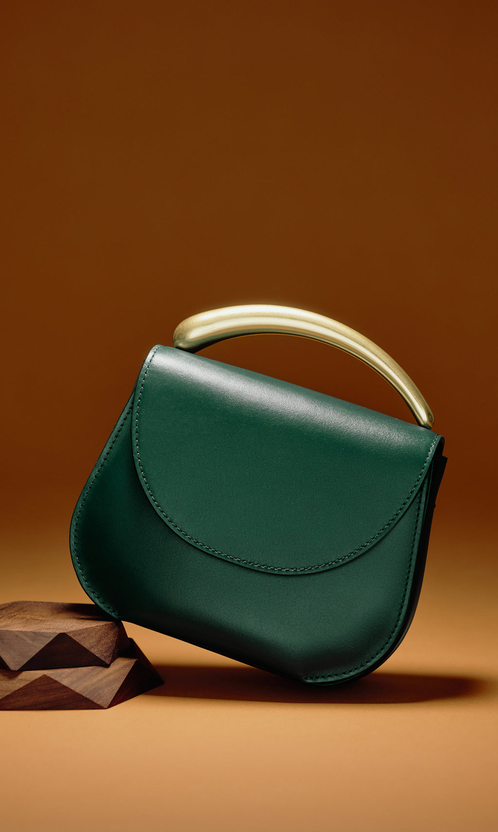 Handbag with a curved handle resting on a decorative wooden block.