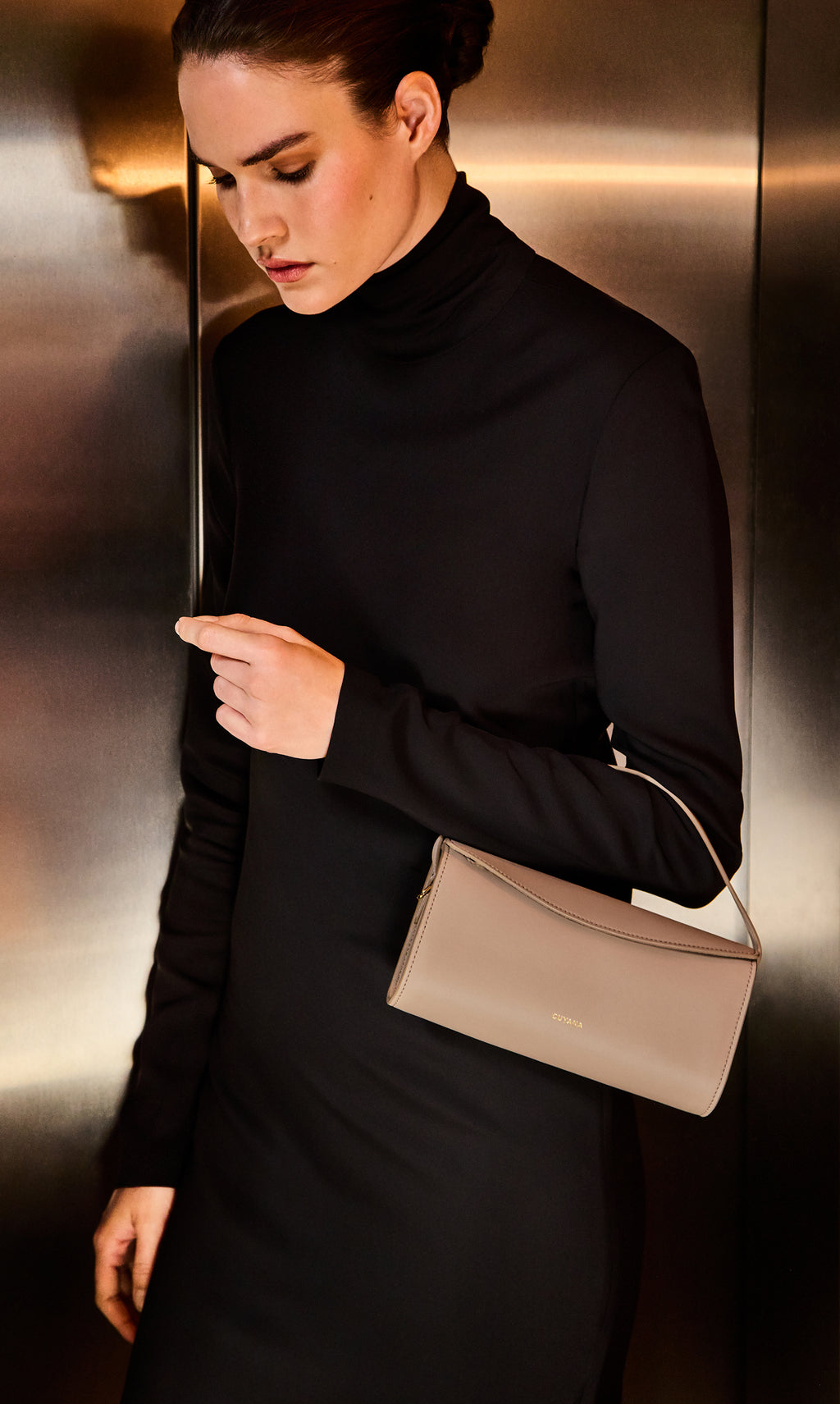Person in turtleneck holding a small handbag in an elevator.