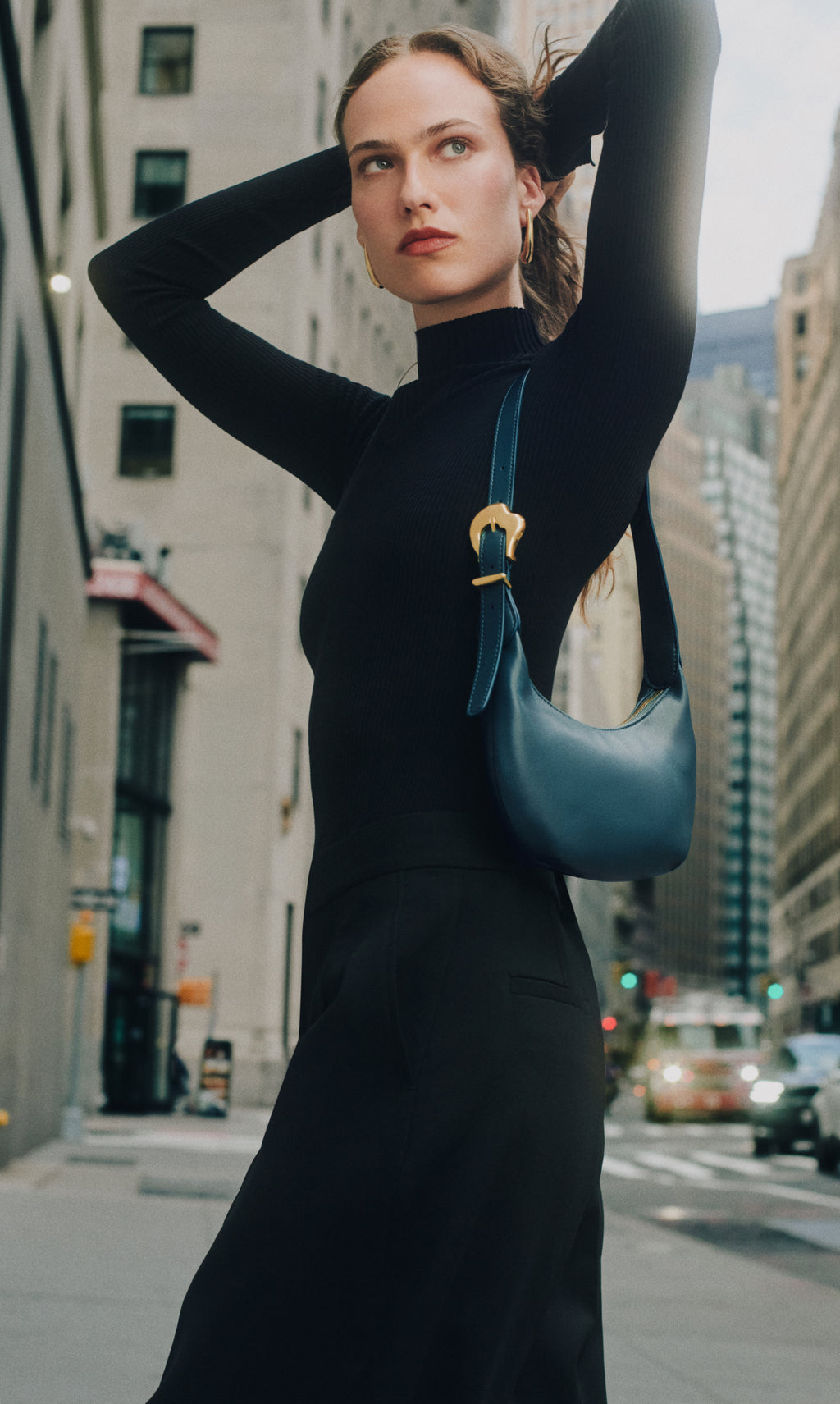 Person in city street with shoulder bag arms raised