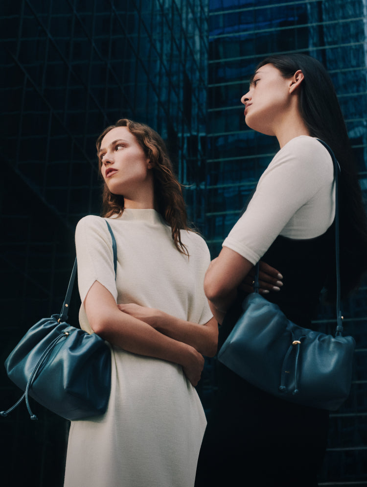 Two people holding handbags, standing in front of tall buildings.