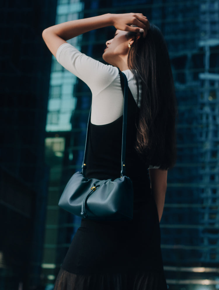 Person with shoulder bag outside near tall buildings.