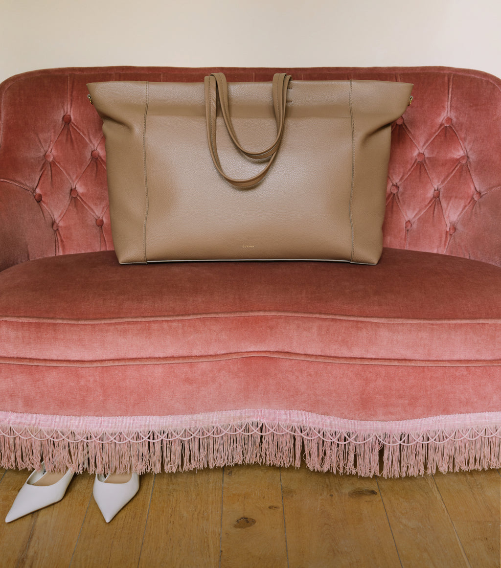 Large tote bag on a tufted sofa with shoes on the floor nearby.