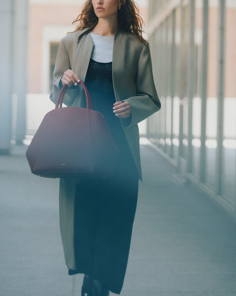 Person walking with a large handbag, wearing a coat over a dress.