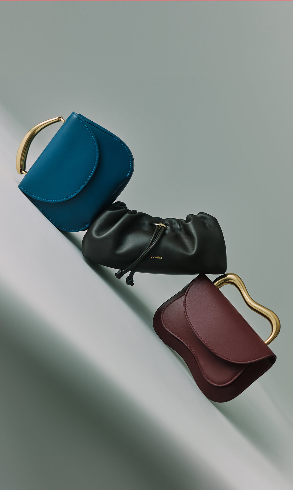 Three handbags with unique handles arranged on a slanted surface.