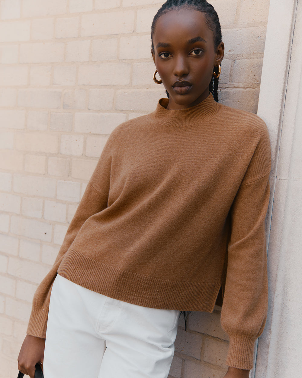 Woman leaning against a wall wearing a sweater and pants.