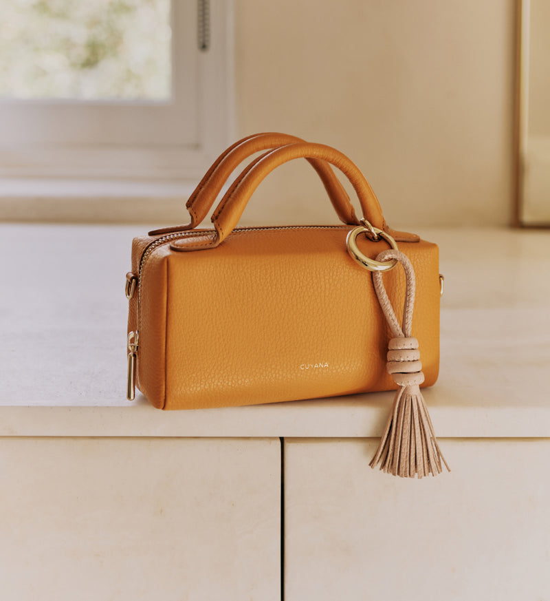Handbag with a handle and a tassel placed on a ledge indoors.