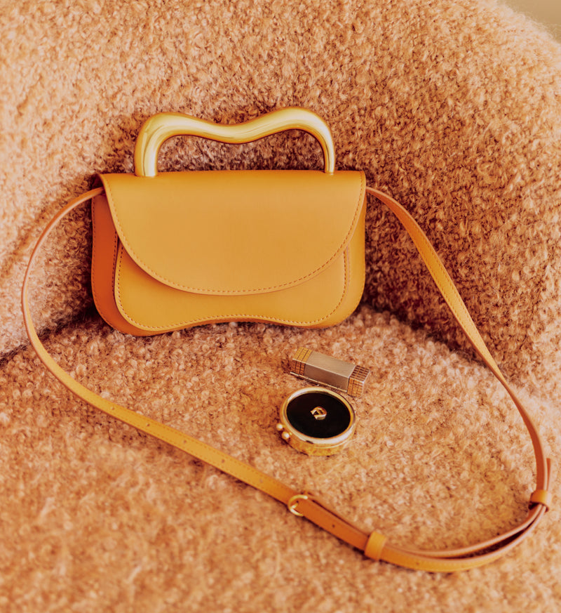Handbag with a curved handle and strap next to a smartwatch on a textured surface.
