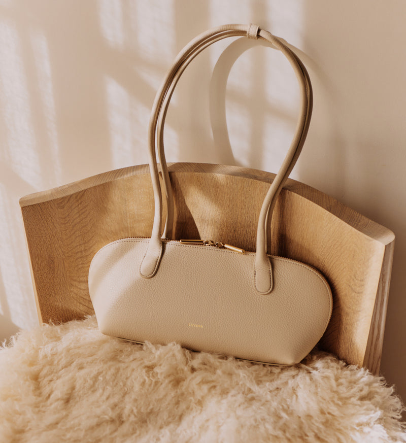 Handbag with long handles on a wooden chair with a soft cushion.