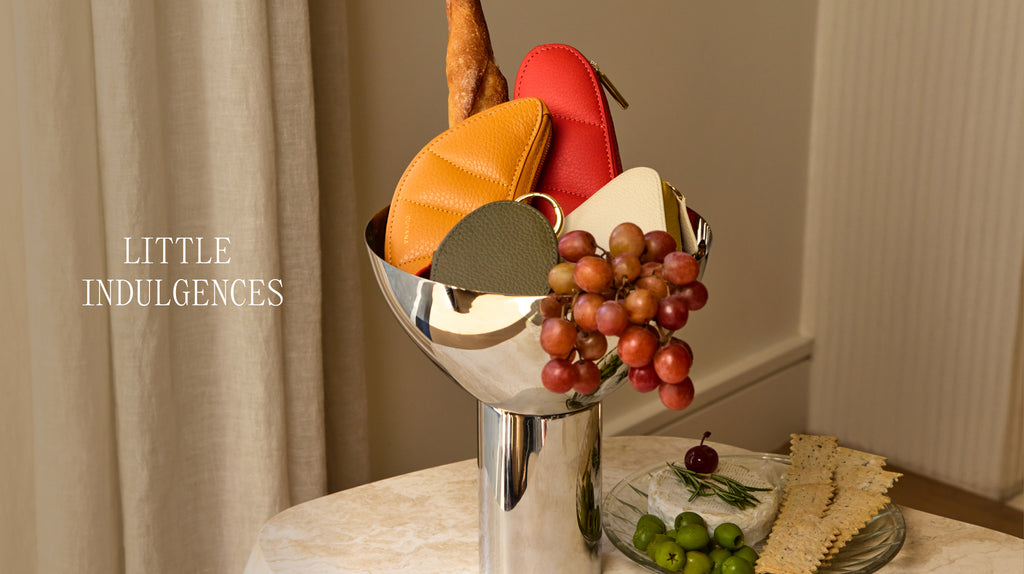 Fruit and small pouches arranged in a silver vase on a table with bread and olives nearby