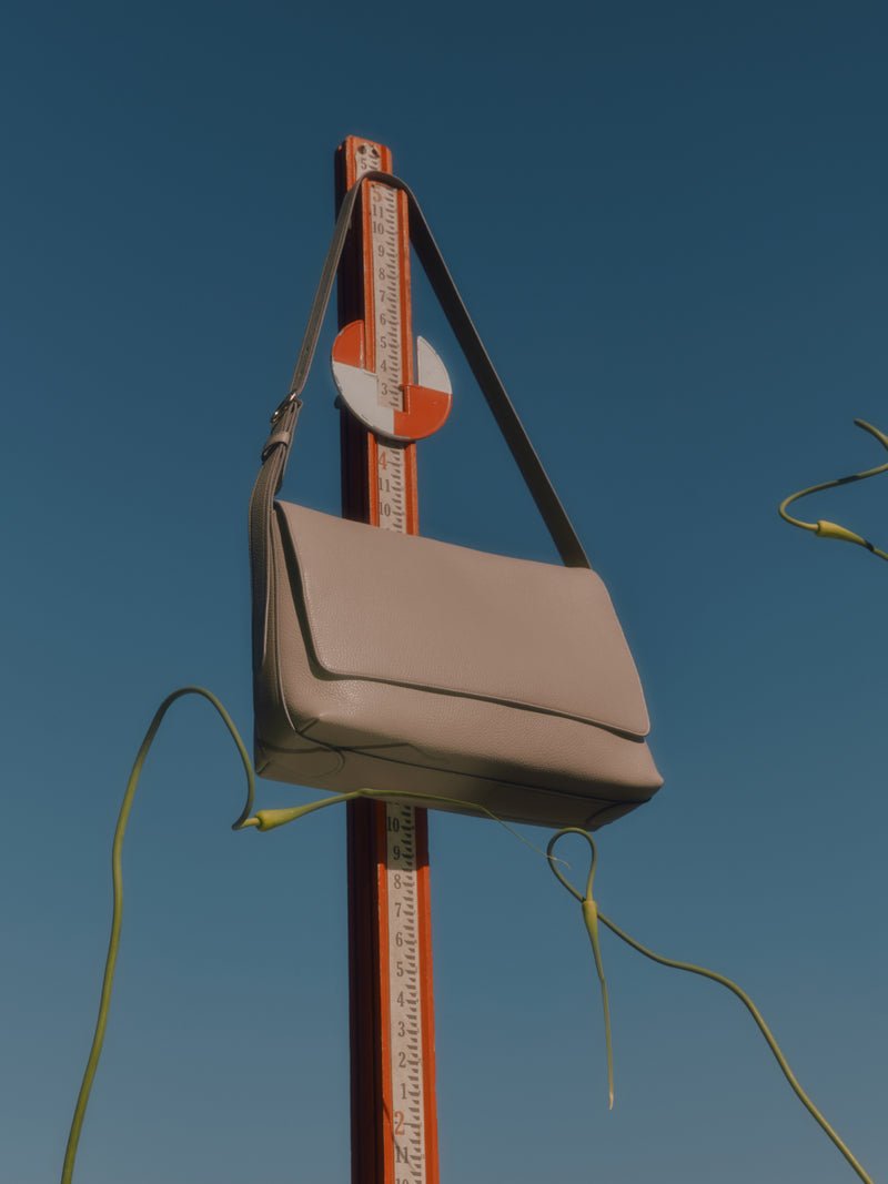 Handbag hanging on a tall measuring stick outdoors with clear sky background.