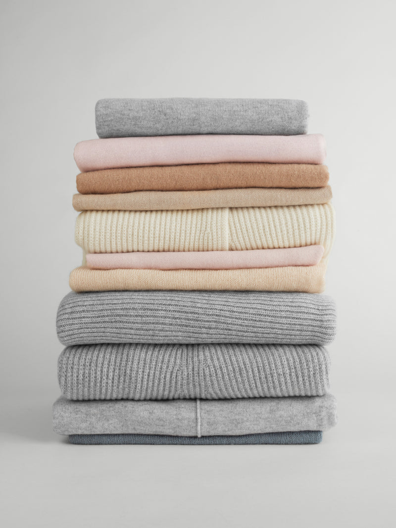 Stack of folded sweaters on a plain background.