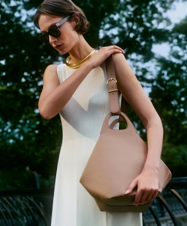 Woman wearing sunglasses and a necklace, holding a large handbag.