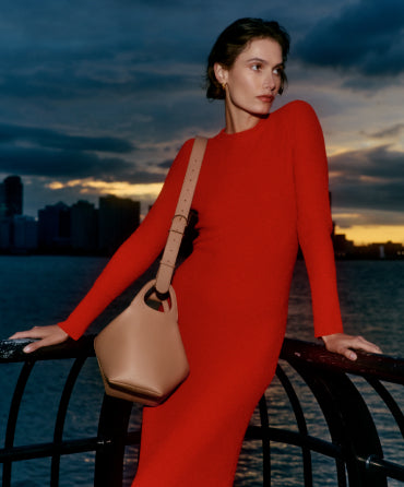 Person leaning against a railing near water holding a bucket bag