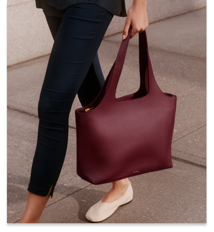 Person carrying large tote bag walking on sidewalk.