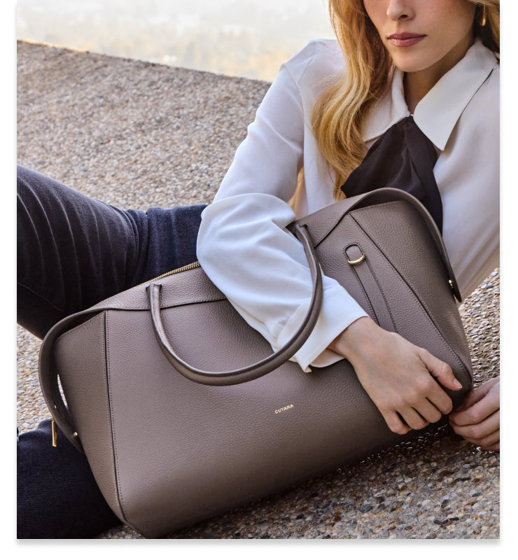 Person holding a large handbag, sitting on a textured surface.
