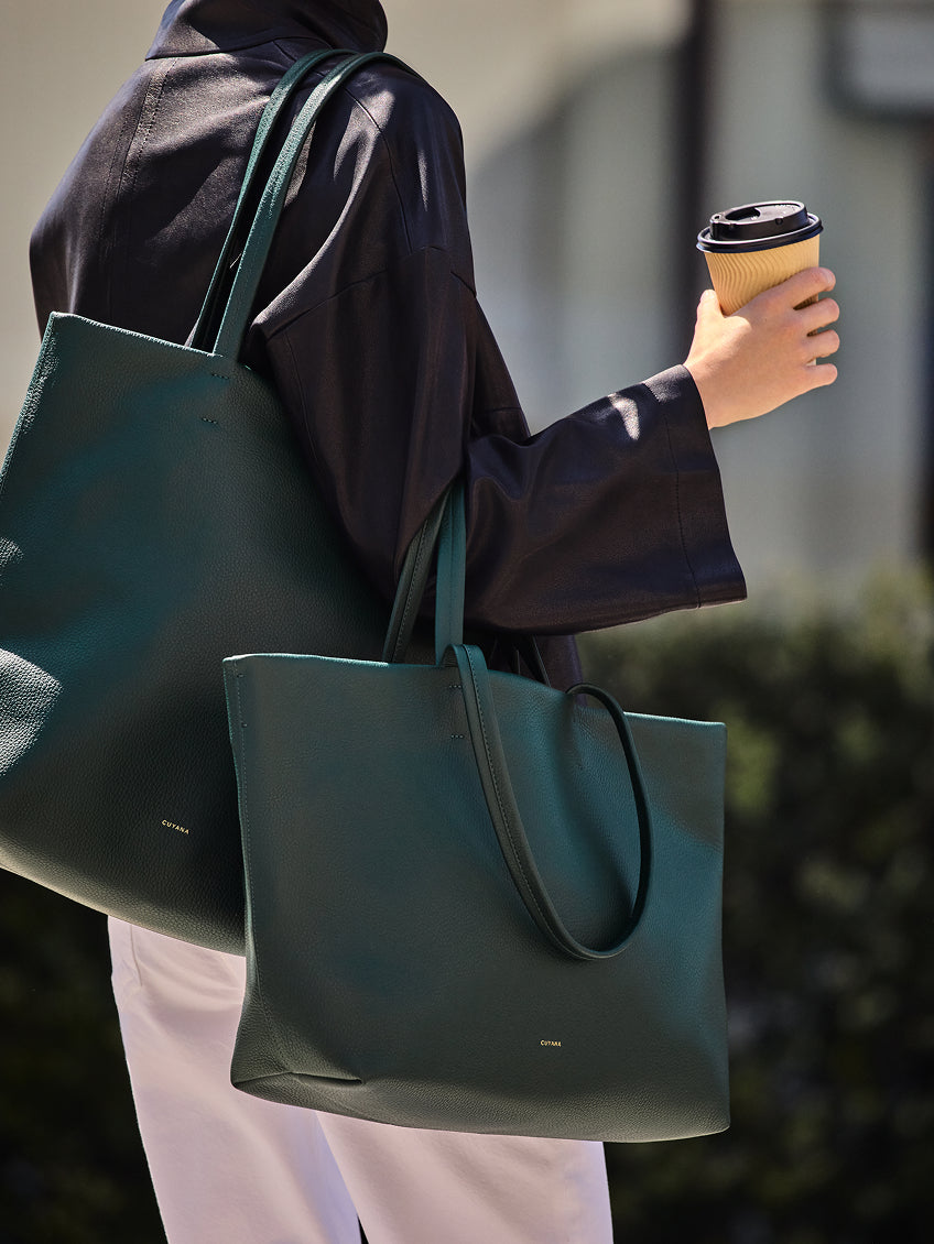 Person holding two tote bags and a coffee cup.