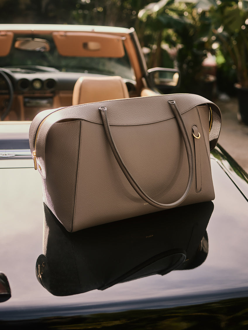 Travel bag on a car hood with convertible in the background.
