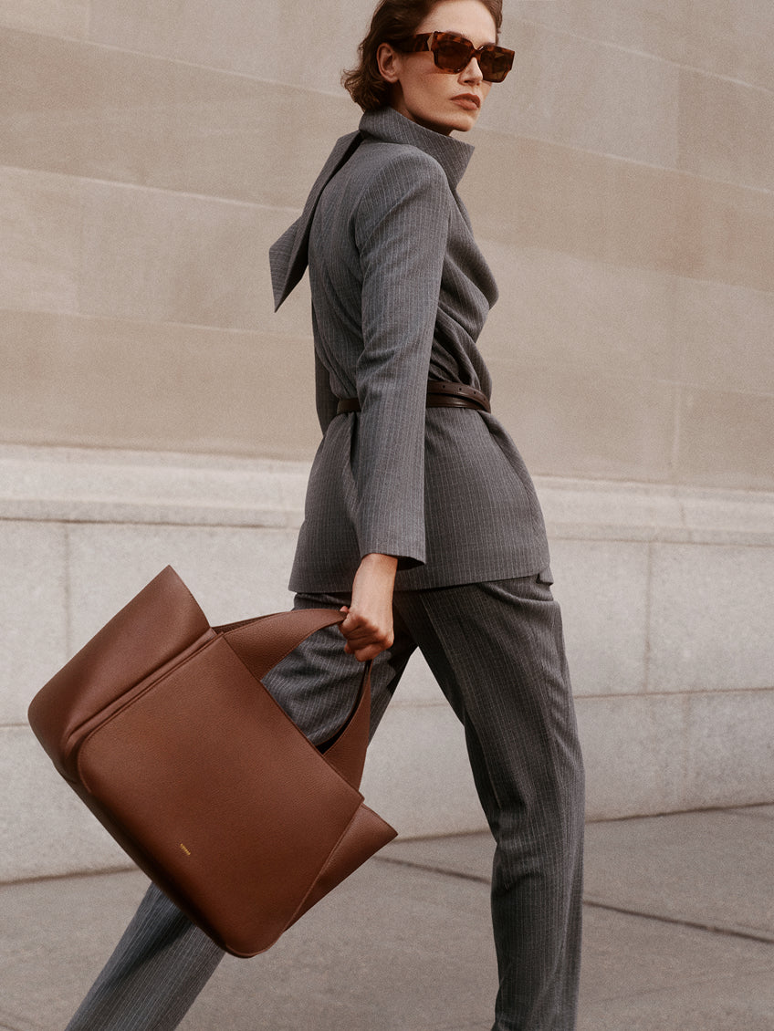 Person in tailored outfit holding a large bag walking outdoors.