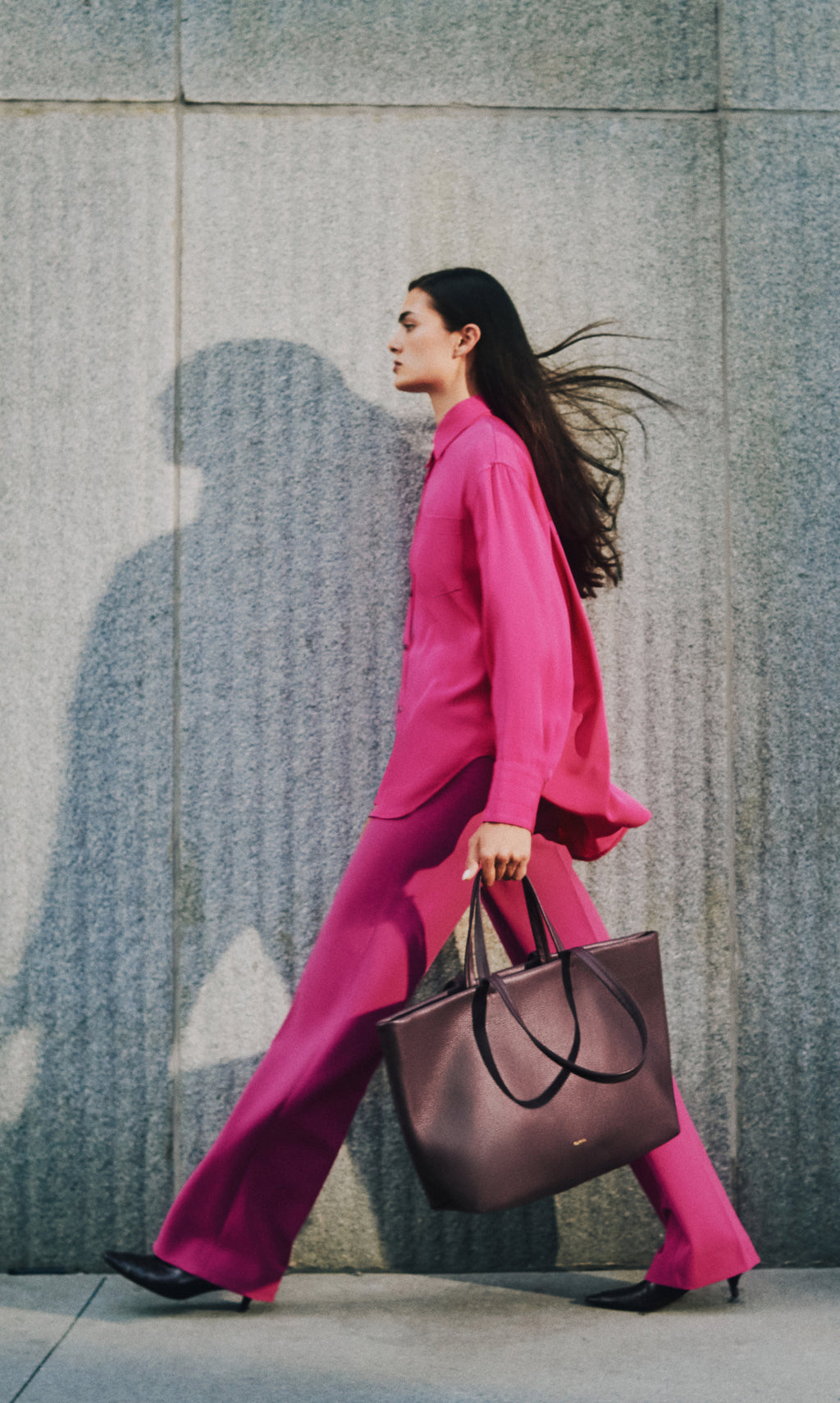 Person walking with a large tote bag in front of a wall.
