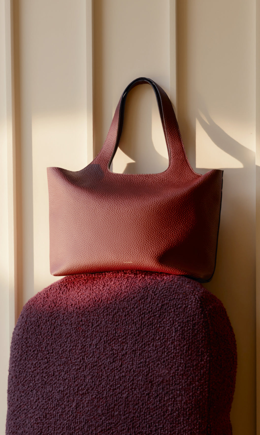 A tote bag resting on a cushioned surface against a paneled wall.