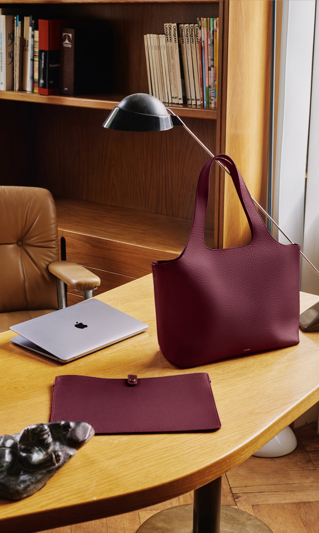 A tote bag, pouch, and laptop on a desk in an office setting.