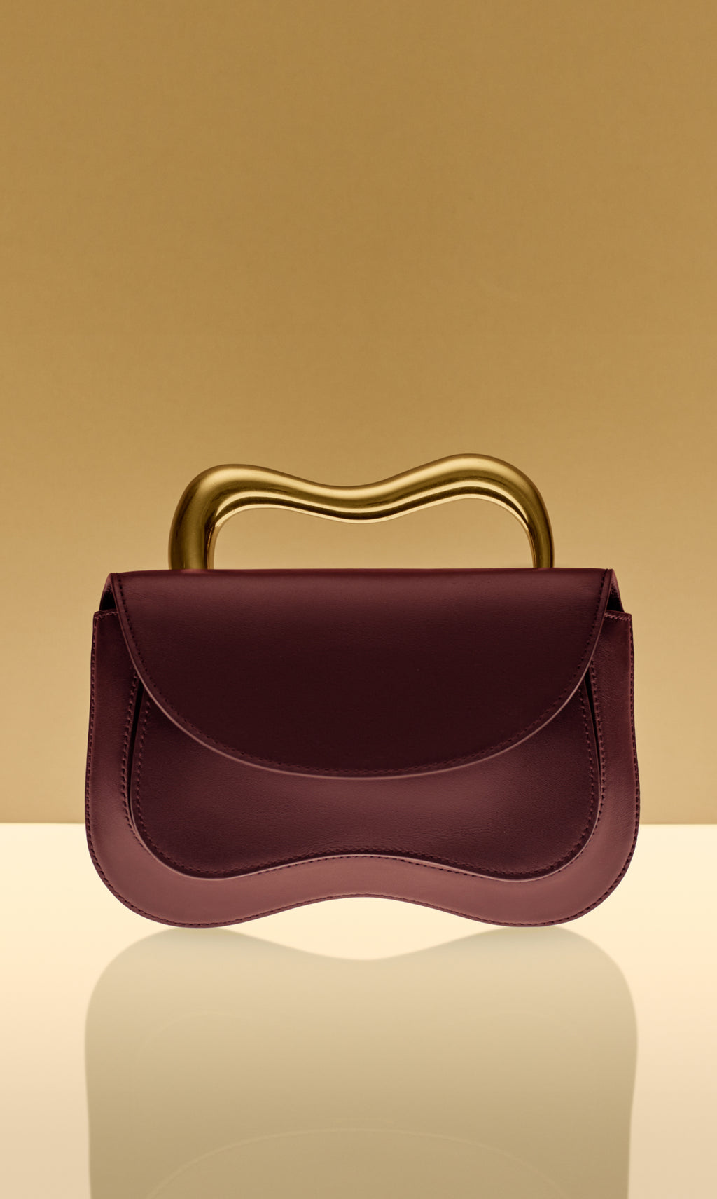 Handbag with wavy metallic handle on reflective surface.