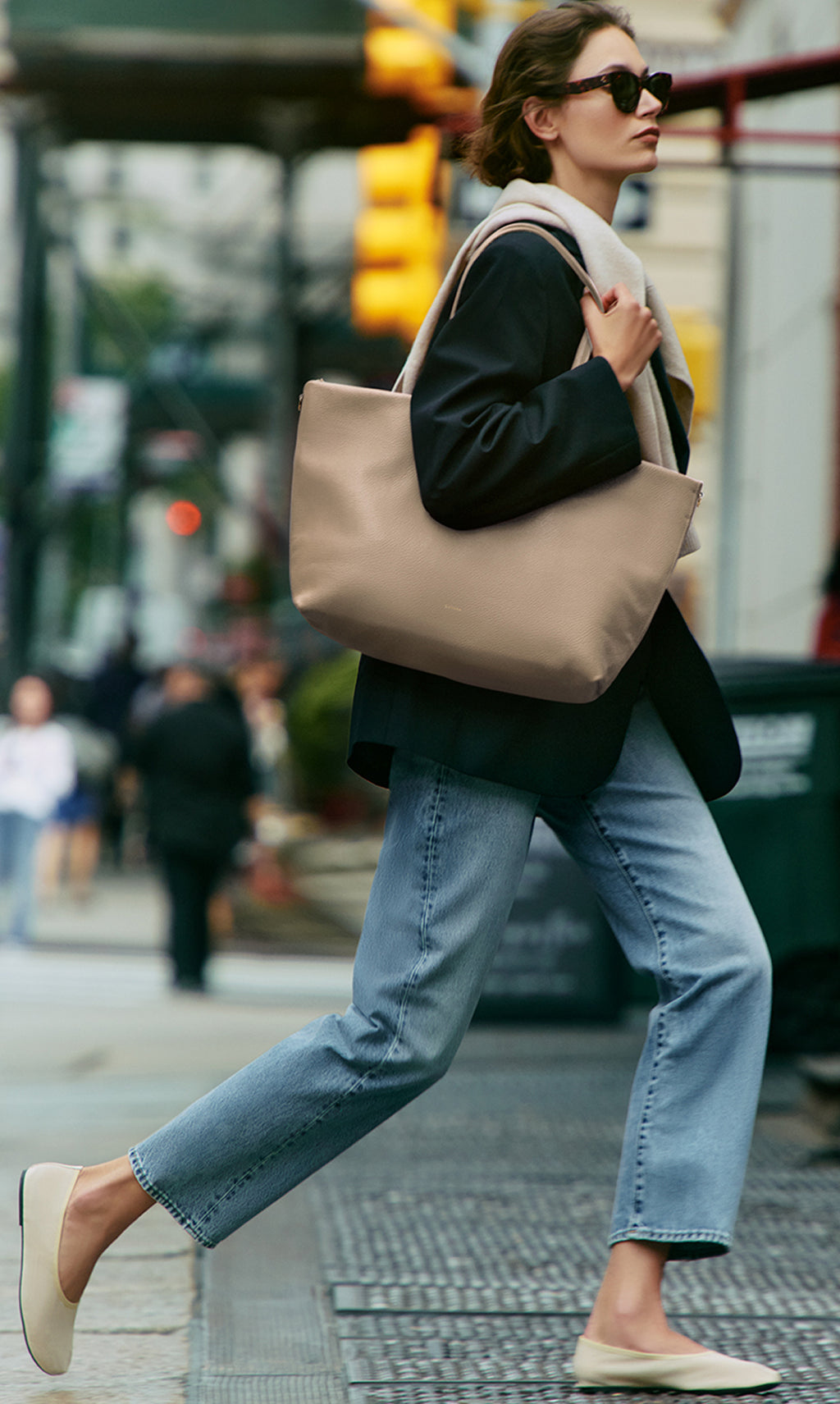 Person walking on a city street carrying a large tote bag over their shoulder.