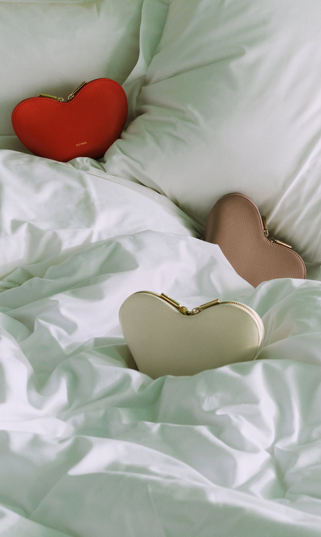 Three heart-shaped purses on a bed with pillows.