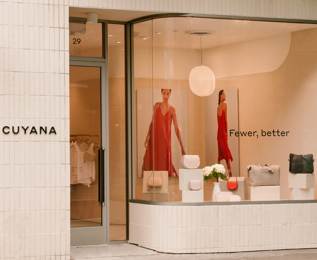 Storefront with mannequins in red dresses, bags displayed on a ledge.