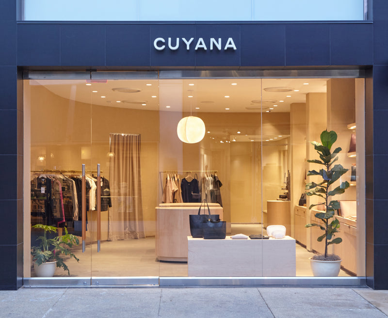 Storefront with clothes inside and plants near the entrance.