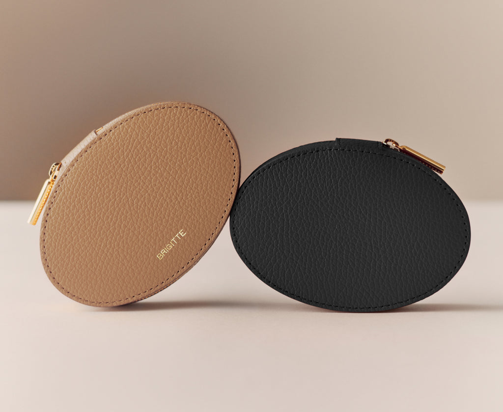 Two oval coin pouches with zippers leaning against each other.