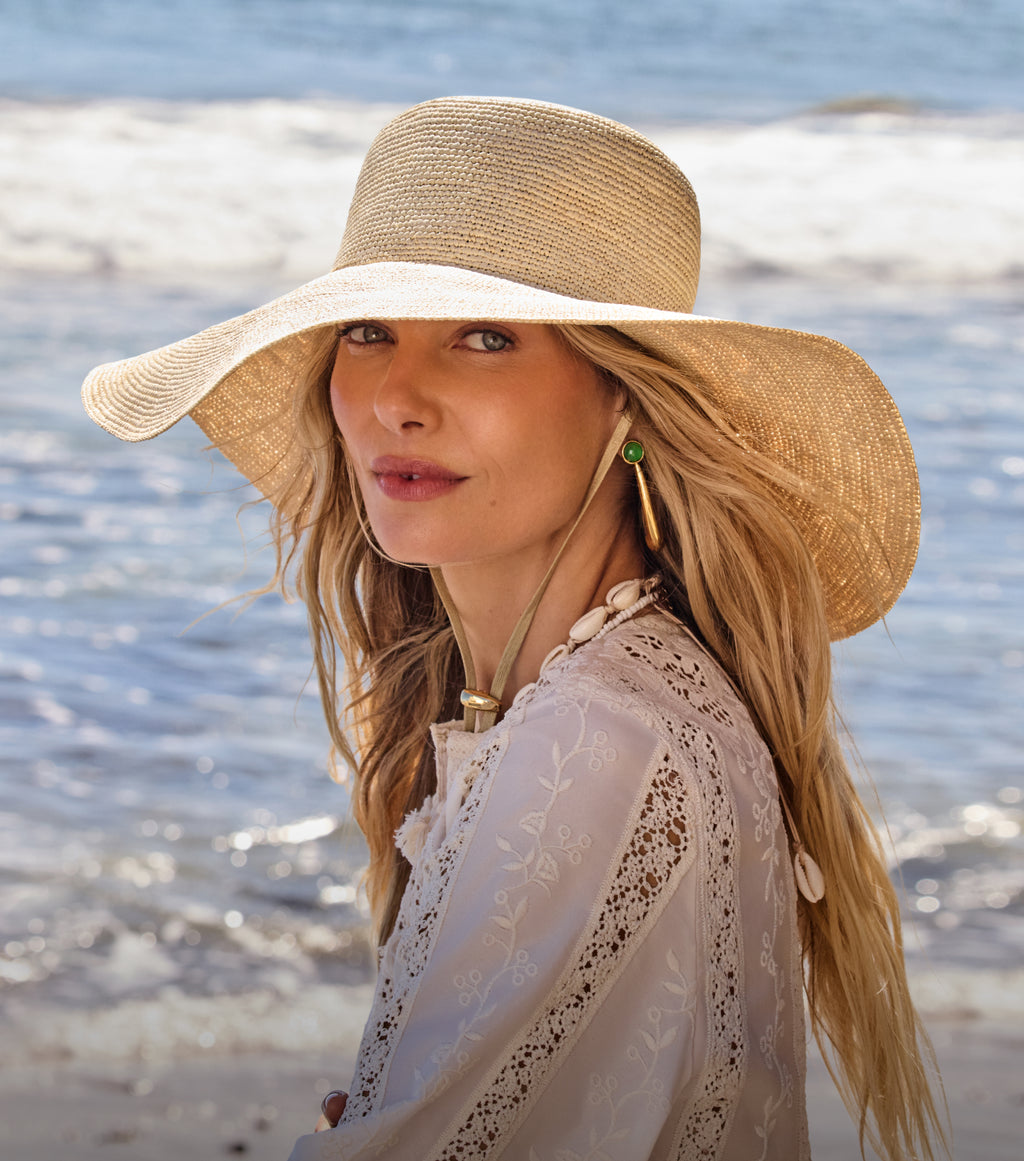 Person wearing wide-brimmed hat on beach with ocean in background.