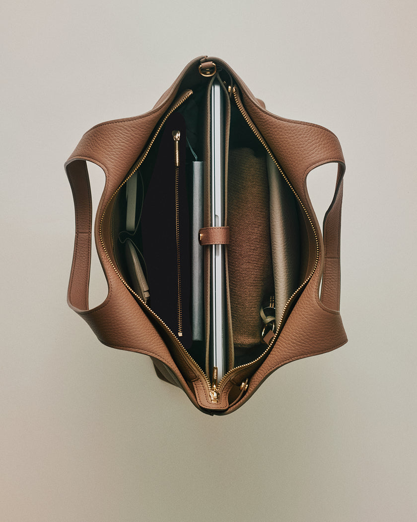 Open handbag with various items inside, including a laptop, notebooks, and a pen.